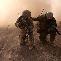 A Special Forces soldier and U.S. Marine Corps Joint Terminal Attack Controller brace for the debris cloud from an approaching CH-53 <i>Super Stallion</i> during a March 2014 tactical recovery exercise.