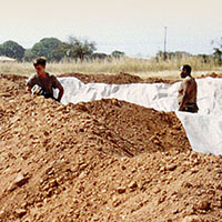 Soldiers connect 4-inch hoses to the 10,000 gallon collapsible fuel bags. The bags are emplaced with the help of U.S. Army Engineers, who build protective berms around the site.