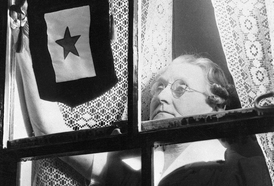 The mother of a WWI serviceman hangs her Blue Star Service banner in her front window