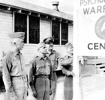 Colonels Charles H. Karlstad (Psychological Warfare Center & School Commandant) and Aaron Bank (Center Executive Officer), along with Lieutenant Colonels Lester L. Holmes (6th RB&L Group commander) and John O. Weaver (Chief of the Psywar Division of the Army General School at Fort Riley, Kansas) pose by the Headquarters sign on Smoke Bomb Hill, Fort Bragg, NC.