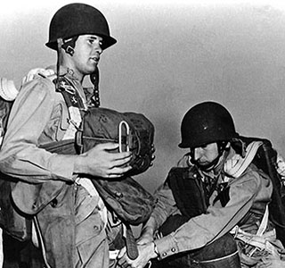 With jumps occurring almost daily, paratroopers in training at Camp Mackall had plenty of opportunities to perfect their pre-jump routine. Notice the large size of the old static lines attached to the soldiers’ parachutes.