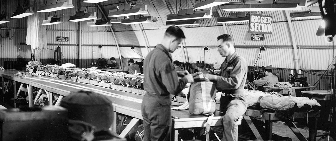 Men of the Rigger Section pack parachutes. Notice the bright lighting which helped to ensure that the parachutes were packed correctly.