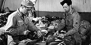 Riggers are stowing the static lines on parachutes that will be attached to canister containers.