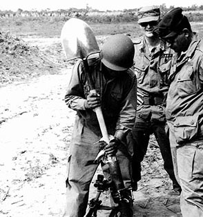 CPT James Trimble and SFC Dan Chapa observe a field expedient method of cleaning a 60 mm mortar.