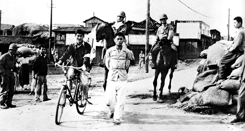 Mounted South Korean soldiers “ride herd” on a prisoner as he is marched through a P’yongyang street to a prisoner-collection point.