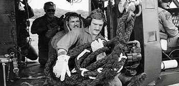 Then-SFC Richard C. Lamb, ODA 795, Company C, 3-7th SFG, prepares a fast rope from a UH-1H Huey helicopter in Panama during training before Operation JUST CAUSE. SFC Christopher R. Zets assists from inside.